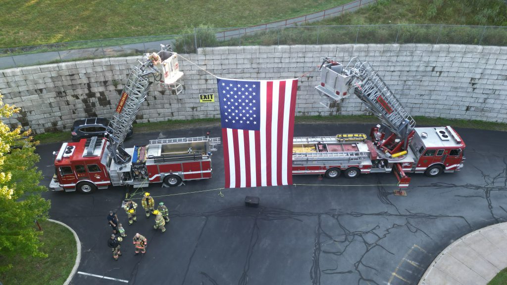 An American Flag is held between two fire trucks as first responders stand near
