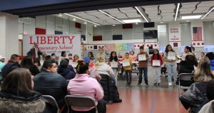 Students hold award certificates in front of a crowd.