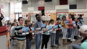 Students hold award certificates in front of a crowd.