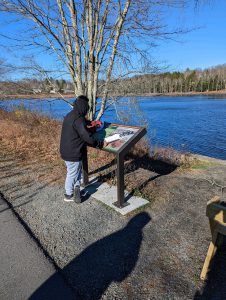 A student reads an informational plaque near a body of water