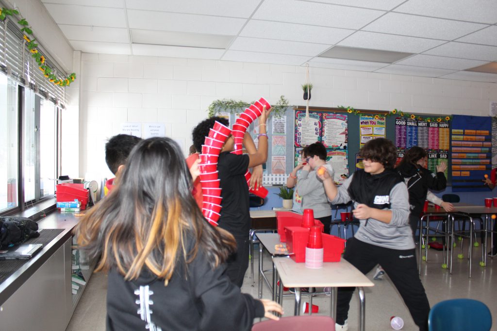 Students maneuver stacked cups to catch a ping pong ball