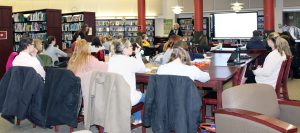 Teachers sit at tables watching a presentation