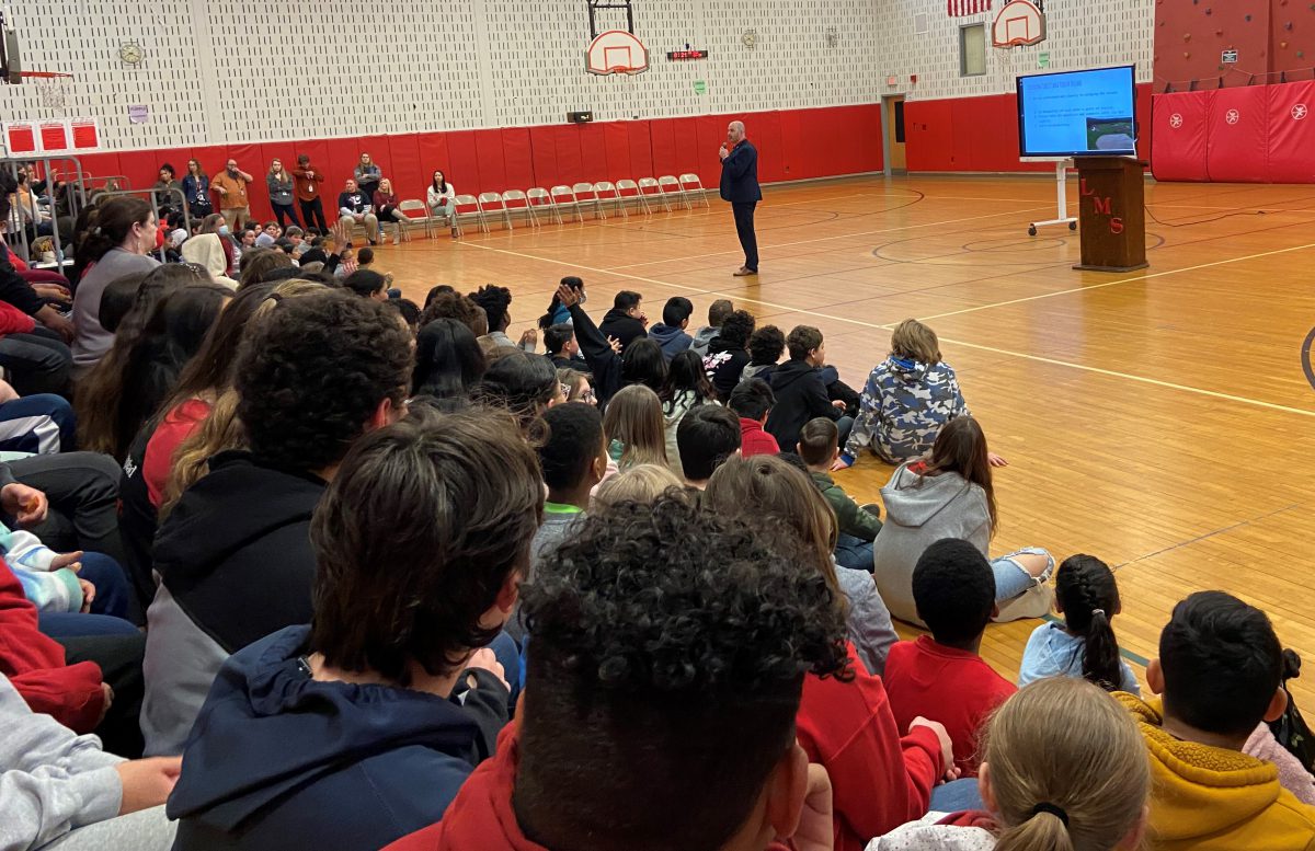 A man speaks in front of students sitting on bleachers