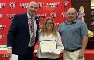 A woman holding a certificate is flanked by two men.