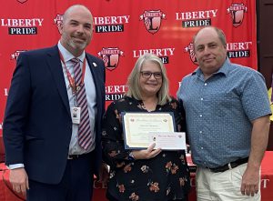A woman holding a certificate is flanked by two men.