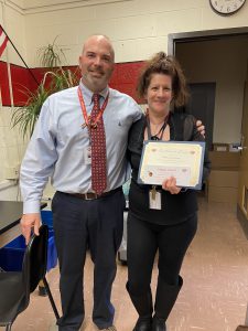 A woman holds a certificate as a man stands next to her with his arm around her shoulders.