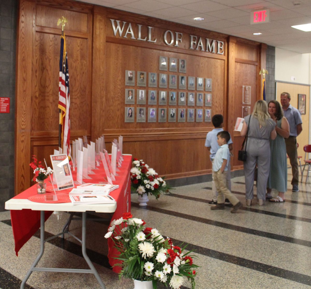 People talk in front of the Wall of Fame as a table sits at right with biographies of all past inductees.