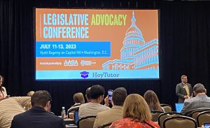 A crowd watches a speak who stands near a display that reads legisltaive Advocacy conference with a drawing of the Capitol building.