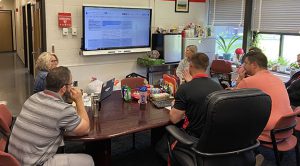 people sit around a desk looking at a screen with a document displayed