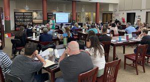 People sit at tables looking at papers and a smart board at the front of the room