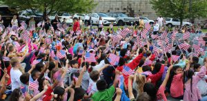 Students seated on the ground wave American flags