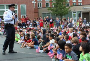 A police officer speaks to children seated in a parking lot.