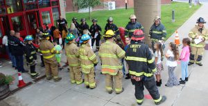 First responders stand in two lines as students wave and give thumbs up as they enter a building