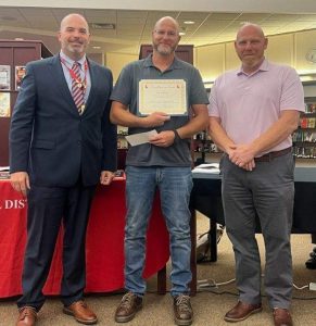 A man holding a certificate is flanked by two other men