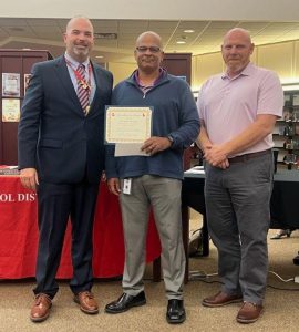 A man holding a certificate is flanked by two other men