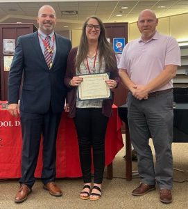 A woman holds a certificate while flanked by two men.