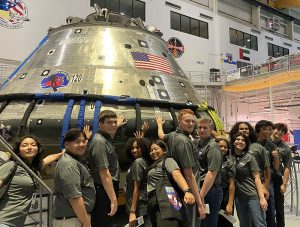 Students in gray shirts put their hands on NASA capsule