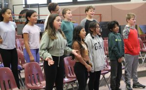 Students stand on risers with chairs behind them and sing