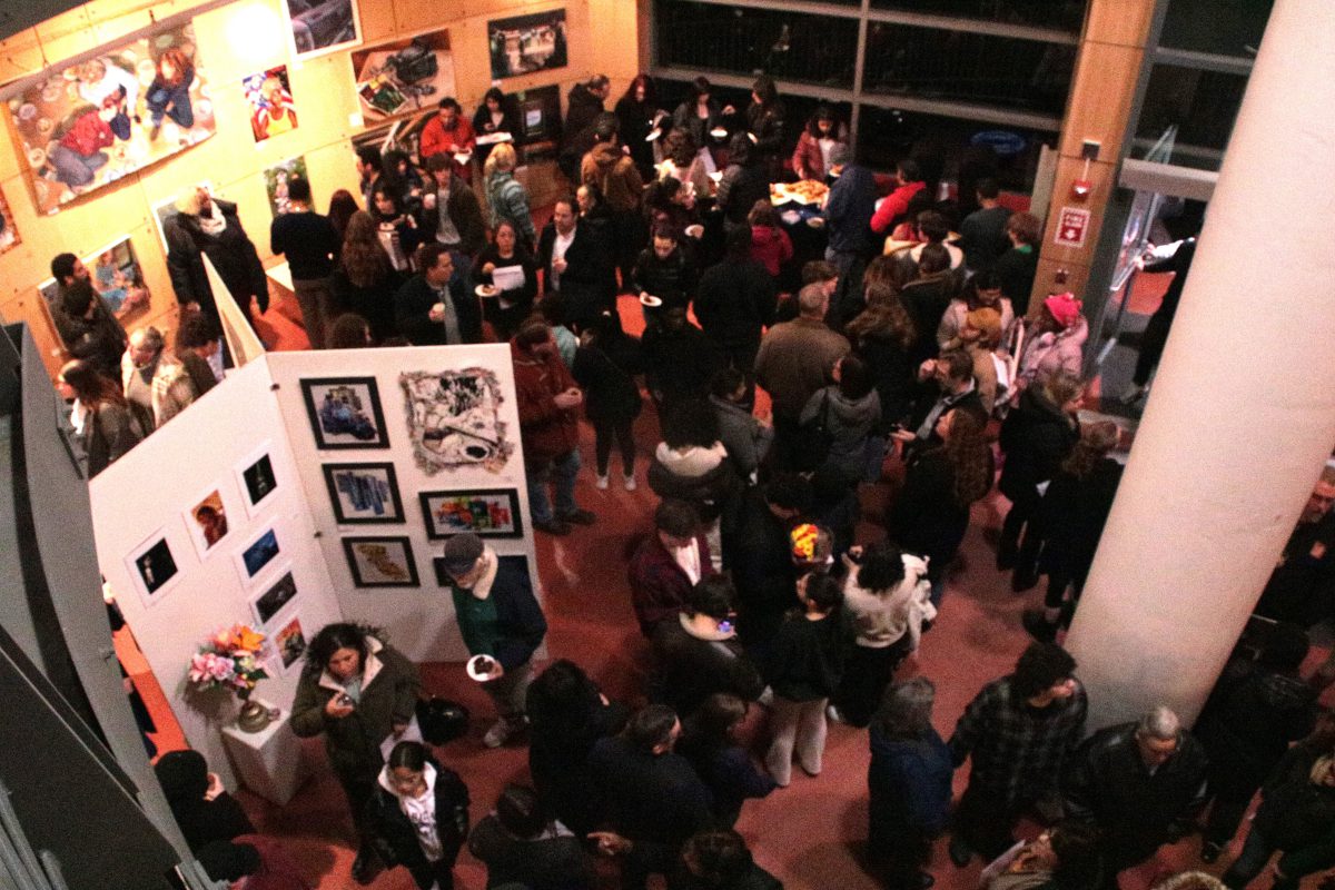 Seen from above, people gather in a gallery space with particians featuring student artwork