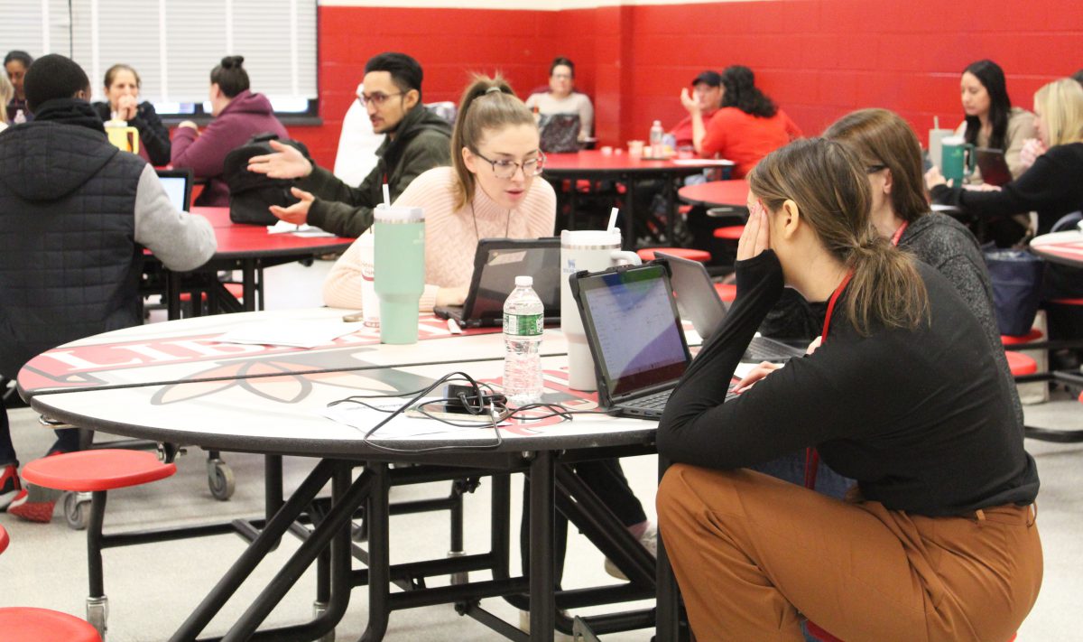 Two teachers work with their Chromebooks while sitting at a circular table.