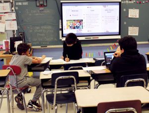 Students work on posters while sitting at or standing near desks