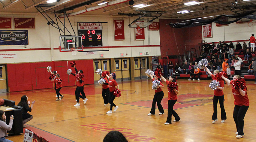 Cheerleaders in red shirts in black pants perform using red and silver pom-poms.