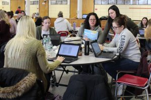 A group of teachers sit at a circular table working on Chromebooks