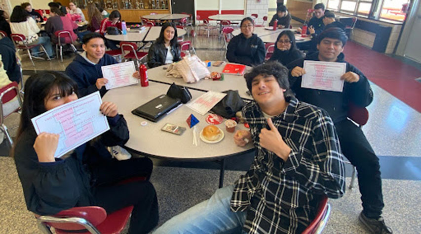 Students pose with honor roll certificates while seated at a round tabe.