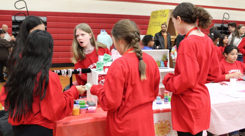 Students in red shirts stand around a craft table and talk