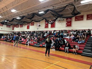 Students and staff sit in the stands in a gymnasium