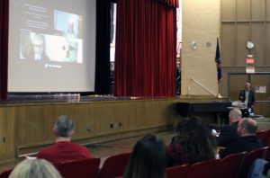 A video shows on a screen at the front of an auditorium.