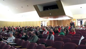 A man speaks at the back of an auditorium as the audience looks ahead at a screen (not shown)