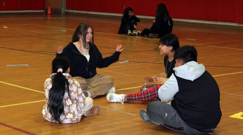 Four students sit in a group on the gym floor