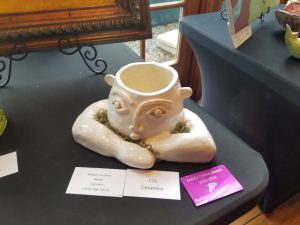 A ceramic sculpture of a face with arms crossed in front of it with cards in front of it