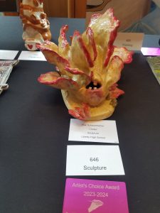 A cream and pink sculpture is on display on a table with cards in front of it