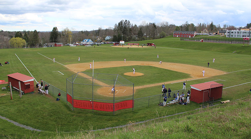 Baseball players are on the field in the foreground with a softball underway in the background