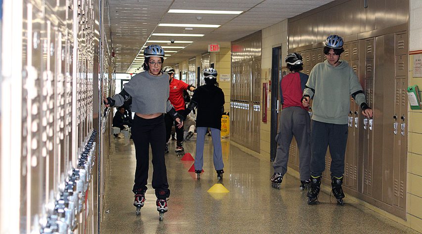 Students rollerblade down a school hallway