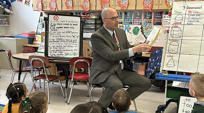 A man reads a book to students in a classroom