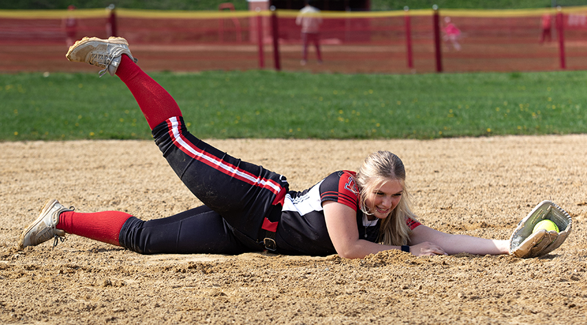 A softball player catches a ball sliding on the diamond