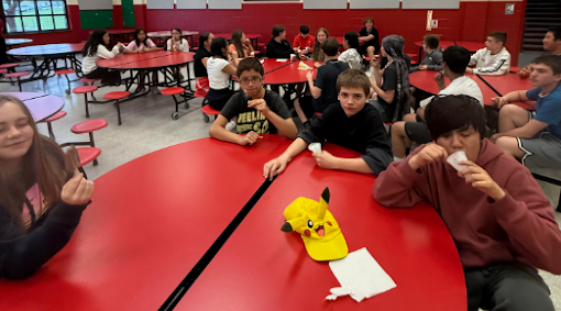 Students sit at round red tables as they eat ice cream.