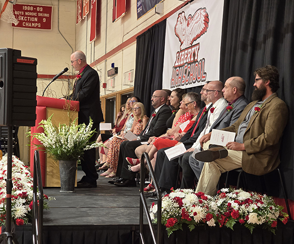 A man speaks on a stage with board members and administrators behind him