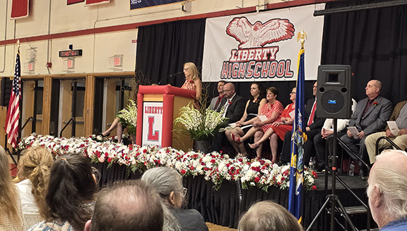 A woman speaks at a podium with board members and administrators behind her