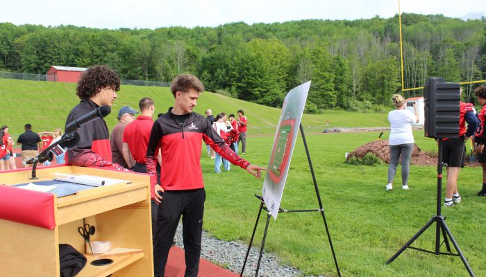 Two students look at the board featuring a drawing of the new field and track