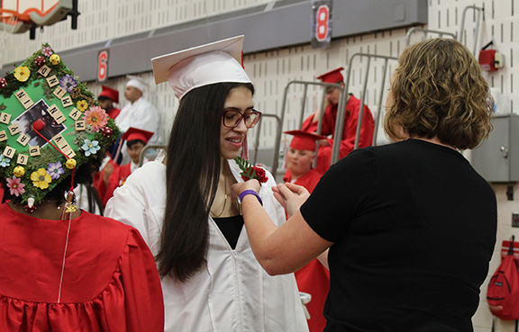 An adult places a flower on a graduates robe.