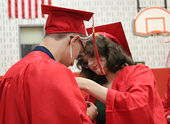 A graduate helps another graduate put a flower on his robe.