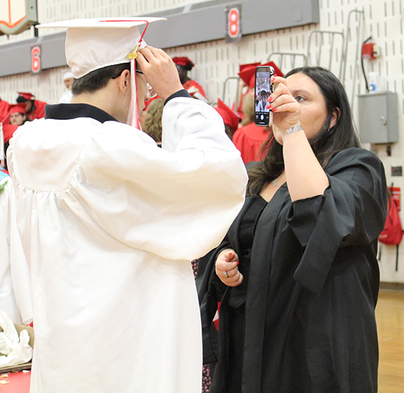 A student looks at at his cap in an adults phone.