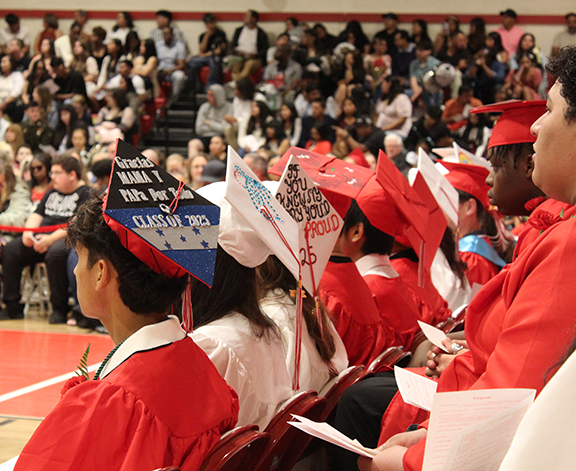 Graduates sit with some with decorated caps