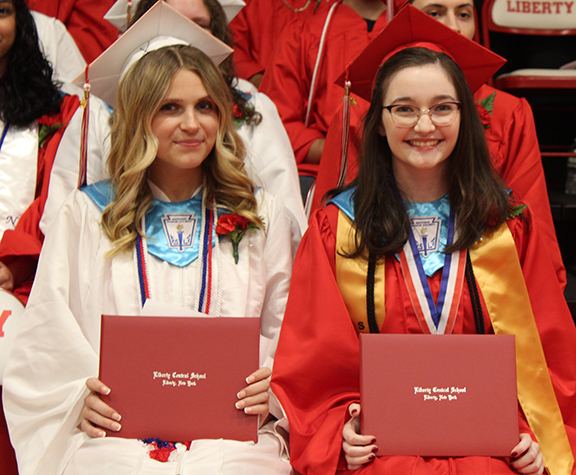 Two students hold their diplomas and smile