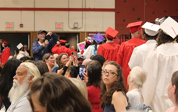 An audience member takes a photo as graduates walk to the stage