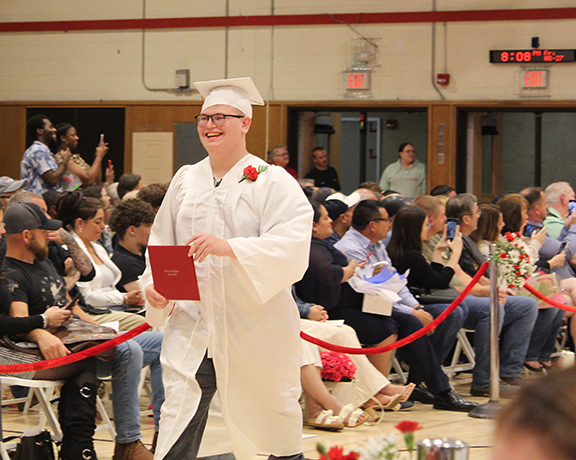 A graduate walks the aisle holds his diploma